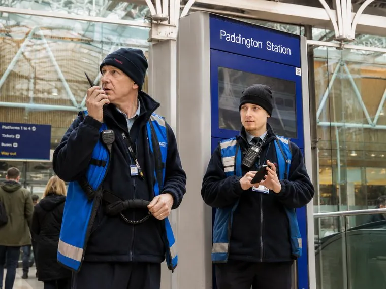 Two members of staff in hi-vis coordinating over radio on a platform